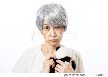 一位表情悲傷的老婦人抱著一隻熊貓毛絨玩具。 139508096