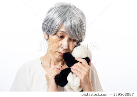 一位神情孤寂的老婦人依偎著一隻熊貓毛絨玩具。 139508097