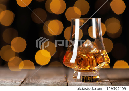 Whiskey in a stylish glass with ice on rustic wood, warm golden bokeh in the background evokes moody, elegant evenings, celebration or relaxed tasting moment Whiskey in a stylish glass with ice on rustic wood, warm golden bokeh in the background evokes moody, elegant evenings, celebration or relaxed tasting moment 139509409
