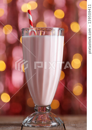 Strawberry milkshake with striped red straw in tall glass, serving as cool refreshing dessert beverage, sitting on wooden table with sparkling bokeh lights Strawberry milkshake with striped red straw in tall glass, serving as cool refreshing dessert beverage, sitting on wooden table with sparkling bokeh lights 139509411