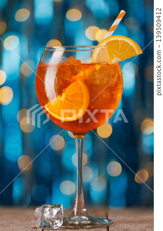 Aperol spritz cocktail with orange slice and ice on rustic wooden table, festive blue and golden bokeh lights evoke holiday happy hour, refreshment and celebration Aperol spritz cocktail with orange slice and ice on rustic wooden table, festive blue and golden bokeh lights evoke holiday happy hour, refreshment and celebration 139509412