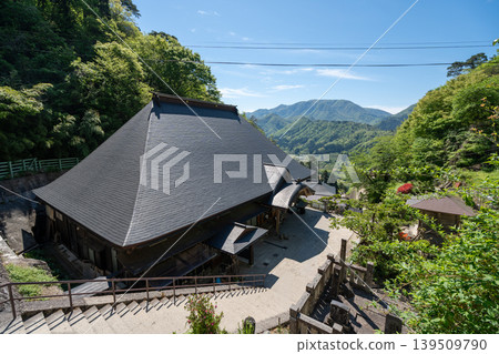 A traditional Japanese temple building in Yamagata, Yamadera, with a large tiled roof and views of the mountain valley. A traditional Japanese temple building in Yamagata, Yamadera, with a large tiled roof and views of the mountain valley. 139509790