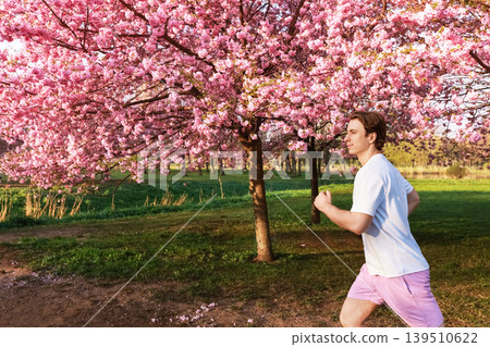 Active man jogging in a scenic park under blooming pink cherry blossoms. Healthy lifestyle, spring fitness, and outdoor exercise concept. 139510622