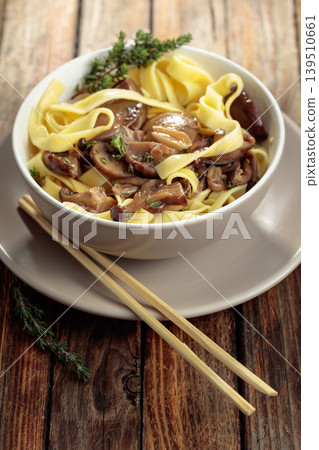 Shimeji and shiitake mushrooms stir-fried with soy sauce, garlic and thyme, served with noodles in a ceramic bowl. Shimeji and shiitake mushrooms stir-fried with soy sauce, garlic and thyme, served with noodles in a ceramic bowl. 139510661