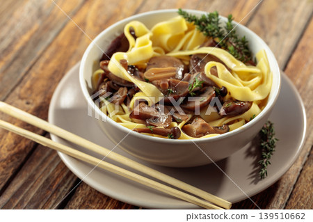 Shimeji and shiitake mushrooms stir-fried with soy sauce, garlic and thyme, served with noodles in a ceramic bowl. 139510662