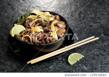 Shimeji and shiitake mushrooms stir-fried with soy sauce, garlic and thyme, served with noodles and lime slice in a black ceramic bowl. Shimeji and shiitake mushrooms stir-fried with soy sauce, garlic and thyme, served with noodles and lime slice in a black ceramic bowl. 139510664