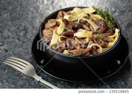 Shimeji and shiitake mushrooms stir-fried with soy sauce, garlic and thyme, served with noodles in a black ceramic bowl. Shimeji and shiitake mushrooms stir-fried with soy sauce, garlic and thyme, served with noodles in a black ceramic bowl. 139510665