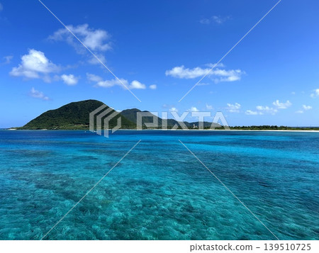 The coral reefs of Iheya Island are visible through the crystal-clear emerald sea and the surrounding green mountains. The coral reefs of Iheya Island are visible through the crystal-clear emerald sea and the surrounding green mountains. 139510725