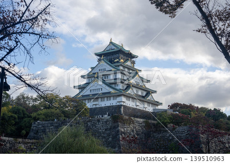 Osaka Castle framed by autumn leaves under a cloudy sky. 139510963