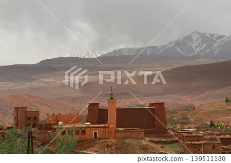 Remote desert village with traditional earthen buildings and snow-capped mountains in background. Remote desert village with traditional earthen buildings and snow-capped mountains in background. 139511180