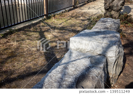 A granite bench in the park, cast by the shadow of an iron fence. A granite bench in the park, cast by the shadow of an iron fence. 139511249
