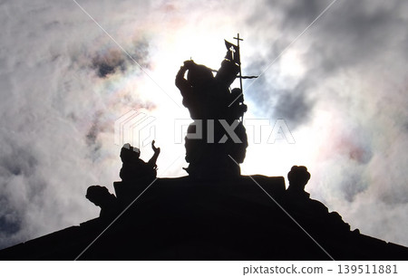 Silhouette of Saint James the Moor-slayer against the sun of a statue swanging the sword and carrying a banner with the Christian cross. Silhouette of Saint James the Moor-slayer against the sun of a statue swanging the sword and carrying a banner with the Christian cross. 139511881