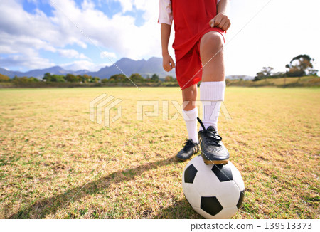 Child, soccer ball and legs on green field for sports, training or practice with clouds and blue sky. Closeup of football player with foot ready for kick off, game or match on outdoor grass in nature Child, soccer ball and legs on green field for sports, training or practice with clouds and blue sky. Closeup of football player with foot ready for kick off, game or match on outdoor grass in nature 139513373
