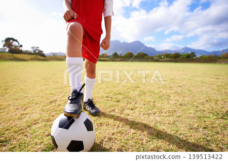 Child, soccer ball and legs on green grass for sports, training or practice with clouds and blue sky. Closeup of football player with foot ready for kick off, game or match on outdoor field in nature 139513422