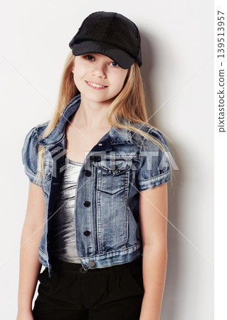 Child, portrait and fashion in studio, cool and confidence by white background. Female person, girl and casual clothing or style by backdrop, kid and denim jacket pride or smiling for trendy cap 139513957