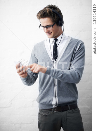 Man, headphones and listening to sound and phone for music by wall background, online and peace. Male person, smartphone and streaming radio or podcast, social media and hearing song on mobile app Man, headphones and listening to sound and phone for music by wall background, online and peace. Male person, smartphone and streaming radio or podcast, social media and hearing song on mobile app 139514319