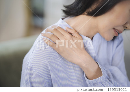 The hands of a woman in her 40s holding her shoulder. 139515021