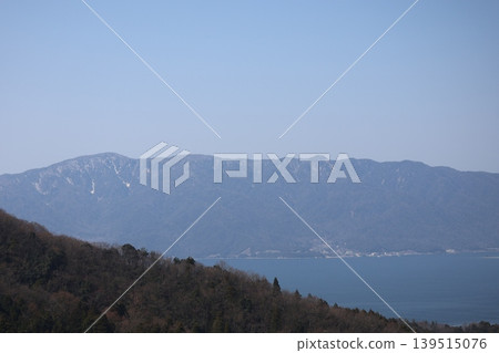 一幅風景畫，畫面中有藍天、連綿的山脈、沿海小鎮、蔚藍的大海，以及前景中的山巒。 139515076