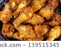 Close-Up of Hot and Spicy Grilled Chicken Drumettes with Glossy Glaze Piled High in a Dark Bowl, Showing Tender Juicy Meat with Rich Golden-Orange Color 139515345