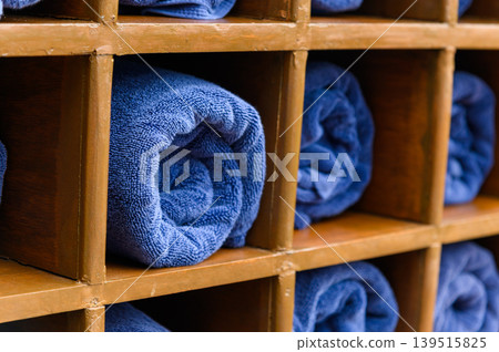 Rolled blue bath towels in wooden box shelf for travellers at swimming pool, sea beach, gym fitness in resort hotel concept. Rolled blue bath towels in wooden box shelf for travellers at swimming pool, sea beach, gym fitness in resort hotel concept. 139515825