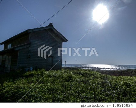 A fishing village on a small hill overlooking the sea, with tiled roof houses, the sun, and the sparkling ocean along the coastline of the Sea of Japan in Akita. A fishing village on a small hill overlooking the sea, with tiled roof houses, the sun, and the sparkling ocean along the coastline of the Sea of Japan in Akita. 139515924