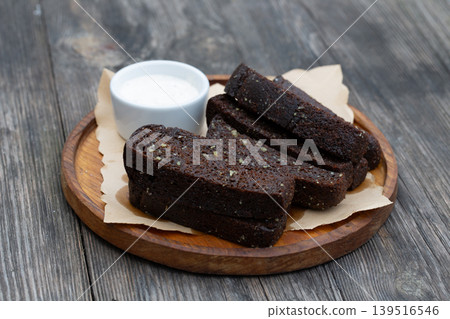 Black garlic bread appetizer with white sauce on a wooden board. Black garlic bread appetizer with white sauce on a wooden board. 139516546