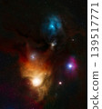 A deep space view features colorful gas clouds in blue, orange, and magenta hues surrounding bright stars and dark nebulae against a dense star field. Telescope live. 139517771