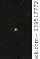 A dense globular star cluster containing thousands of glowing stars is positioned against the dark backdrop of outer space. 139517772