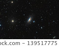 A astrophotography image of the edge-on lenticular galaxy NGC 5078 featuring a prominent dark dust lane and a nearby companion galaxy set against a dense field of distant stars. Telescope live. 139517775