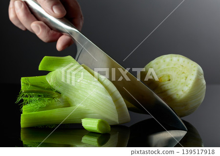 Hand with knife and cut fennel bulb. Hand with knife and cut fennel bulb. 139517918