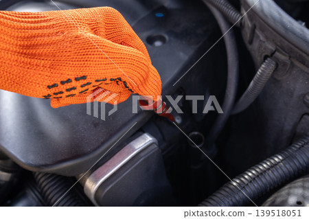 A person uses a dipstick to check the oil level in a car engine while working in a garage during the day A person uses a dipstick to check the oil level in a car engine while working in a garage during the day 139518051
