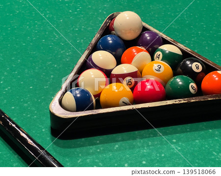 Players prepare for a game of billiards with numbered balls set in a triangle on a green table at a game center during the evening hours Players prepare for a game of billiards with numbered balls set in a triangle on a green table at a game center during the evening hours 139518066
