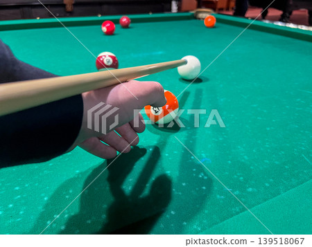 A player focuses on the cue ball on the green felt pool table while preparing to take a shot during a game with friends A player focuses on the cue ball on the green felt pool table while preparing to take a shot during a game with friends 139518067