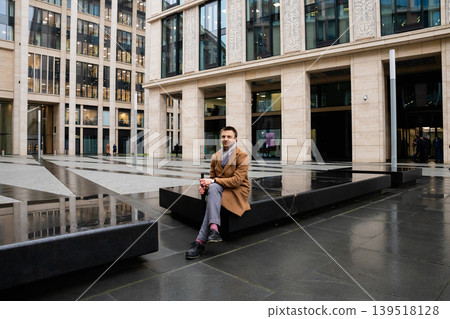 Man sitting on a stone bench in a modern office courtyard. Businessman resting during a break near a city building. Urban lifestyle and corporate architecture in a professional setting. Man sitting on a stone bench in a modern office courtyard. Businessman resting during a break near a city building. Urban lifestyle and corporate architecture in a professional setting. 139518128