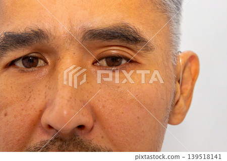 Hispanic man wearing hearing aid in ear. Close up portrait of mature man with hearing loss using modern medical device. Auditory health technology and disability care concept. Hispanic man wearing hearing aid in ear. Close up portrait of mature man with hearing loss using modern medical device. Auditory health technology and disability care concept. 139518141