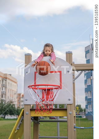 A small preschool-age child throws a basketball into a basket from above. Children's playground in the courtyard A small preschool-age child throws a basketball into a basket from above. Children's playground in the courtyard 139518590