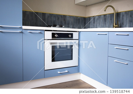 Modern kitchen corner featuring blue cabinetry, a built-in oven, and a stylish faucet, showcasing a contemporary design with clean lines and functional layout Modern kitchen corner featuring blue cabinetry, a built-in oven, and a stylish faucet, showcasing a contemporary design with clean lines and functional layout 139518744