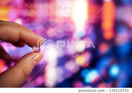 Hand holding a small round gemstone against a colorful blurred background of lights, showcasing the gem's clarity and brilliance in a vibrant setting Hand holding a small round gemstone against a colorful blurred background of lights, showcasing the gem's clarity and brilliance in a vibrant setting 139518785