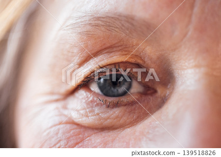 Close-up of an elderly woman blue eye. The face of a mature lady with facial wrinkles and no makeup. Close-up of an elderly woman blue eye. The face of a mature lady with facial wrinkles and no makeup. 139518826