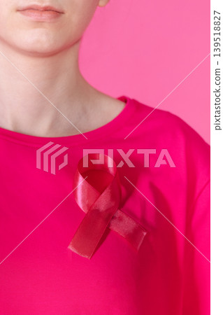 Close-up of a pink satin ribbon as a symbol of the fight against cancer on a woman T-shirt. A girl in pink clothes on a pink background with a ribbon. 139518827