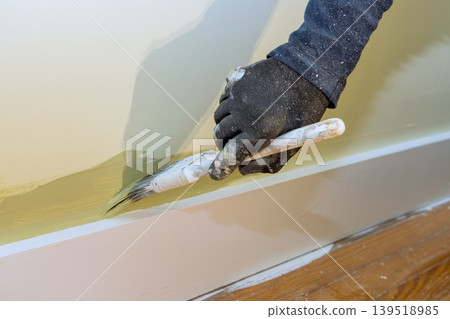 Person paints wall with brush while wearing gloves in room Person paints wall with brush while wearing gloves in room 139518985