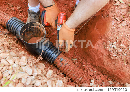 Person works on installing pipes in ground at construction site 139519010
