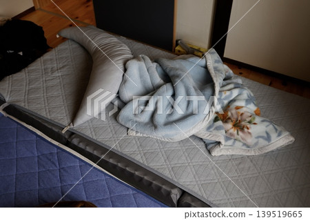 A pillow and blanket left spread out in a dimly lit room. Gray bedding. 139519665