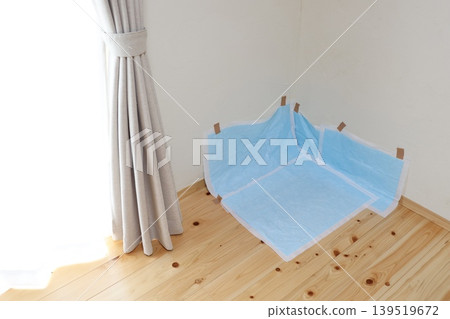 Dog pet training pads. A blue pad taped to the corner of the room. Wooden flooring. 139519672