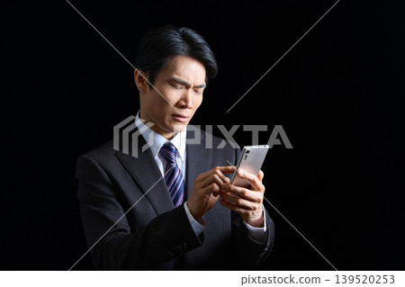 A male office worker struggling with a problem; image of him using his smartphone on a black background. A male office worker struggling with a problem; image of him using his smartphone on a black background. 139520253
