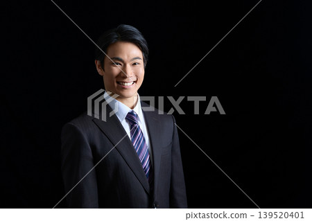Portrait of a smiling young businessman against a black background 139520401