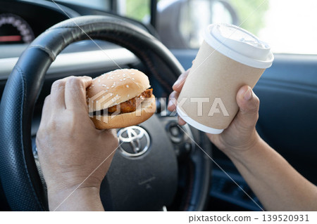 Bangkok, Thailand November 18, 2023 Asian woman driver hold and eat hamburger in car, dangerous and risk an accident. Bangkok, Thailand November 18, 2023 Asian woman driver hold and eat hamburger in car, dangerous and risk an accident. 139520931