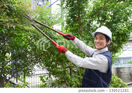 A smiling male worker pruning garden trees. A smiling male worker pruning garden trees. 139521281