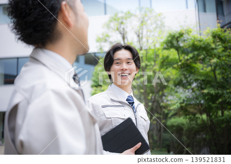 Young workers in work clothes, involved in real estate building maintenance and infrastructure inspection, converse outdoors amidst the fresh greenery. 139521831