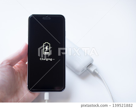 A smartphone with a low battery level is being charged by connecting it to a mobile battery (screen design is original). A smartphone with a low battery level is being charged by connecting it to a mobile battery (screen design is original). 139521882